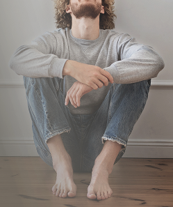 Man sitting on the floor looking upwards, representing reflection and the search for answers regarding intimate health