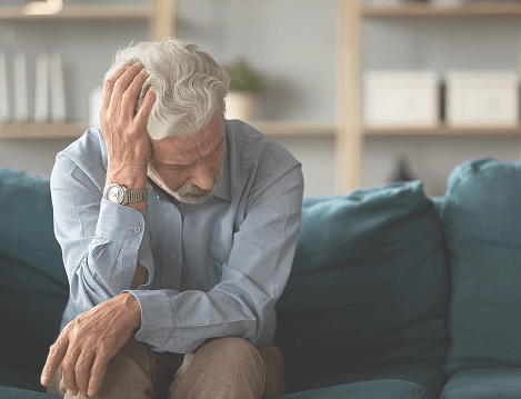 Worried senior man sitting on a sofa with hand on head, representing the emotional distress and burden of intimate health conditions in older age
